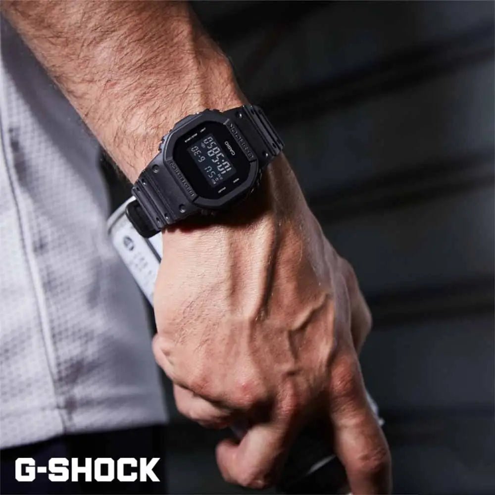 DW-5600BB-1 Casio G-Shock negro mate llevado en muñeca con camisa gris.