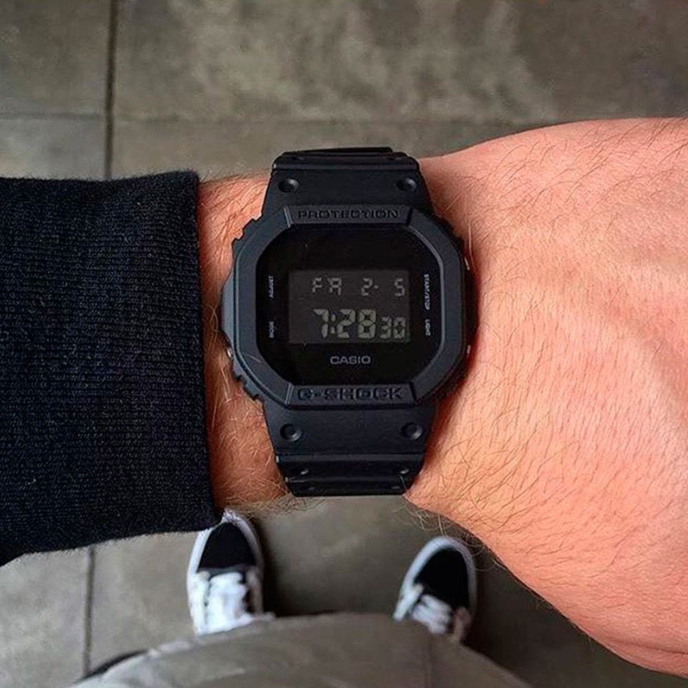 DW-5600BB-1 Casio G-Shock negro en muñeca, con caja rectangular y pantalla digital.
